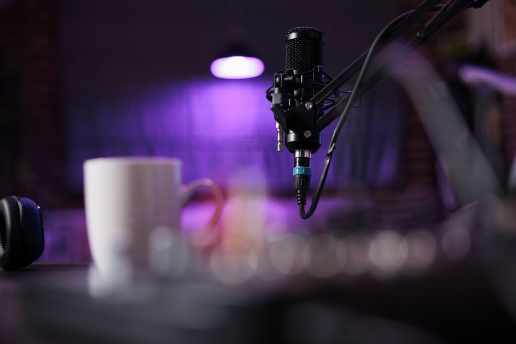 The Content Factory A close-up of a black microphone suspended by a stand, with a white mug and blurred electronic equipment in the foreground, at The Content Factory, all set against a purple-lit background perfect for content creation. In Austin, Texas Ray J Barbershop Customer Acquisition