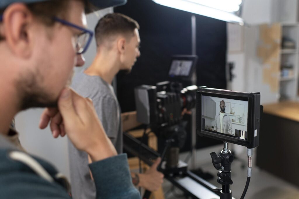 The Content Factory In The Content Factory's podcast studio, two people film a person using a camera and monitor. One operates the camera slider while the other observes the monitor closely, ensuring flawless content creation. In Austin, Texas