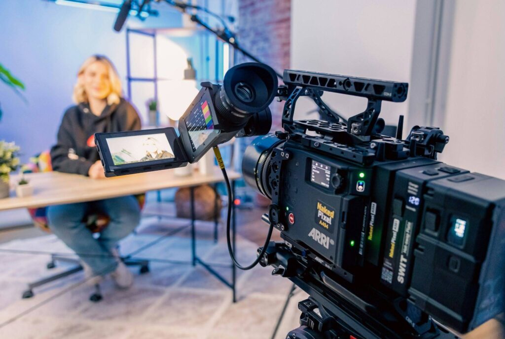 The Content Factory A professional video camera on a set at The Content Factory records a person sitting at a table. The scene includes lighting equipment, a microphone, and decor, making it resemble a high-end podcast studio. The camera's monitor displays a close-up of the person. In Austin, Texas Dentists Social Media Strategy