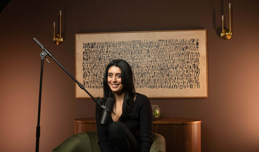 The Content Factory A woman sits in a chair, speaking into a microphone, with abstract art and sconces on the wall behind her. In Austin, Texas