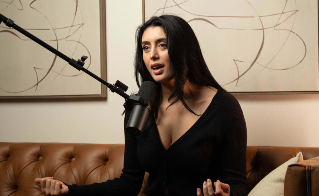 The Content Factory A person with long dark hair speaks into a microphone while seated on a brown sofa, with abstract art in the background. In Austin, Texas
