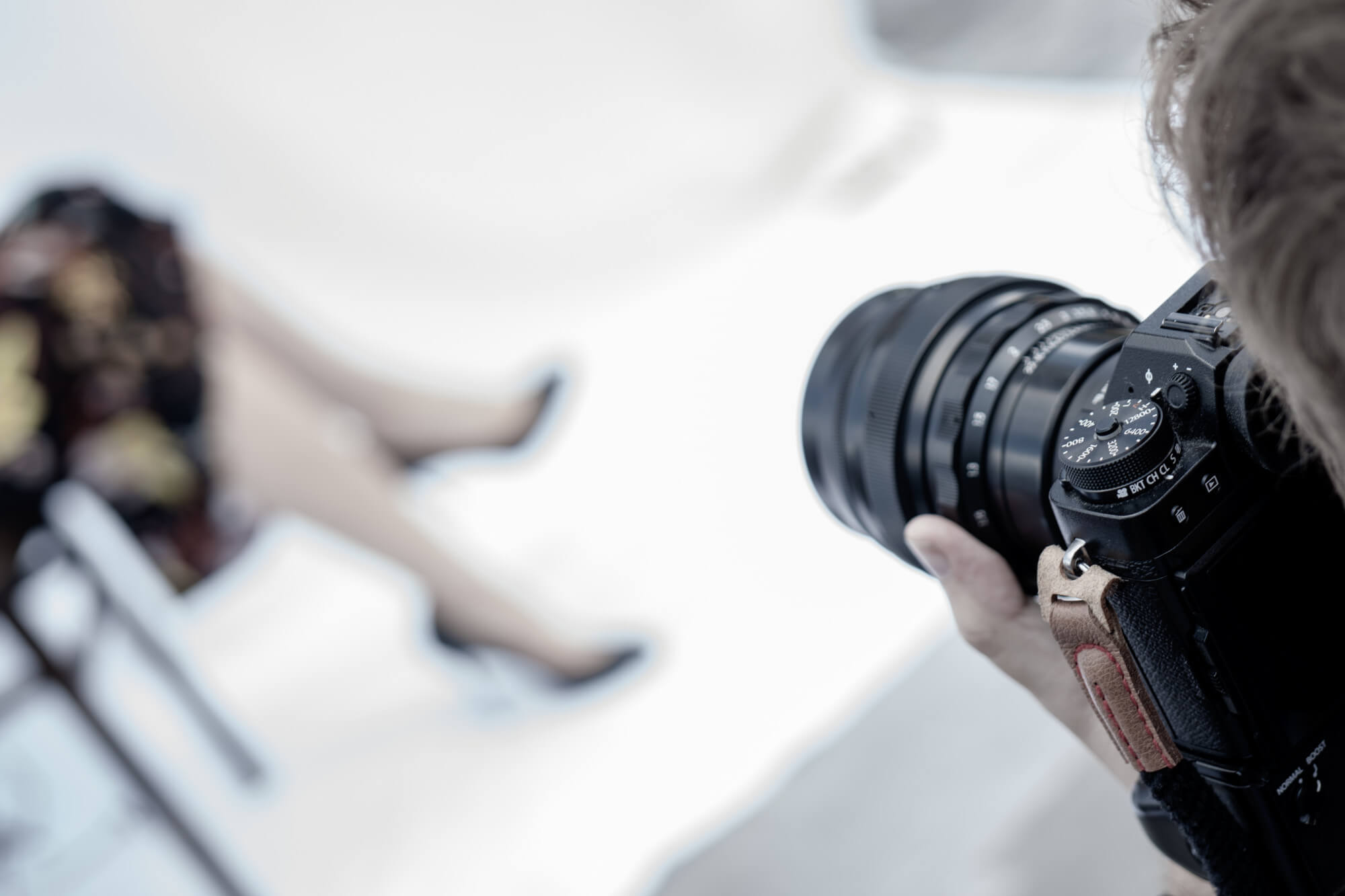 The Content Factory Photographer capturing a seated person wearing a floral skirt and black heels, focusing through a DSLR camera in a studio setting. In Austin, Texas